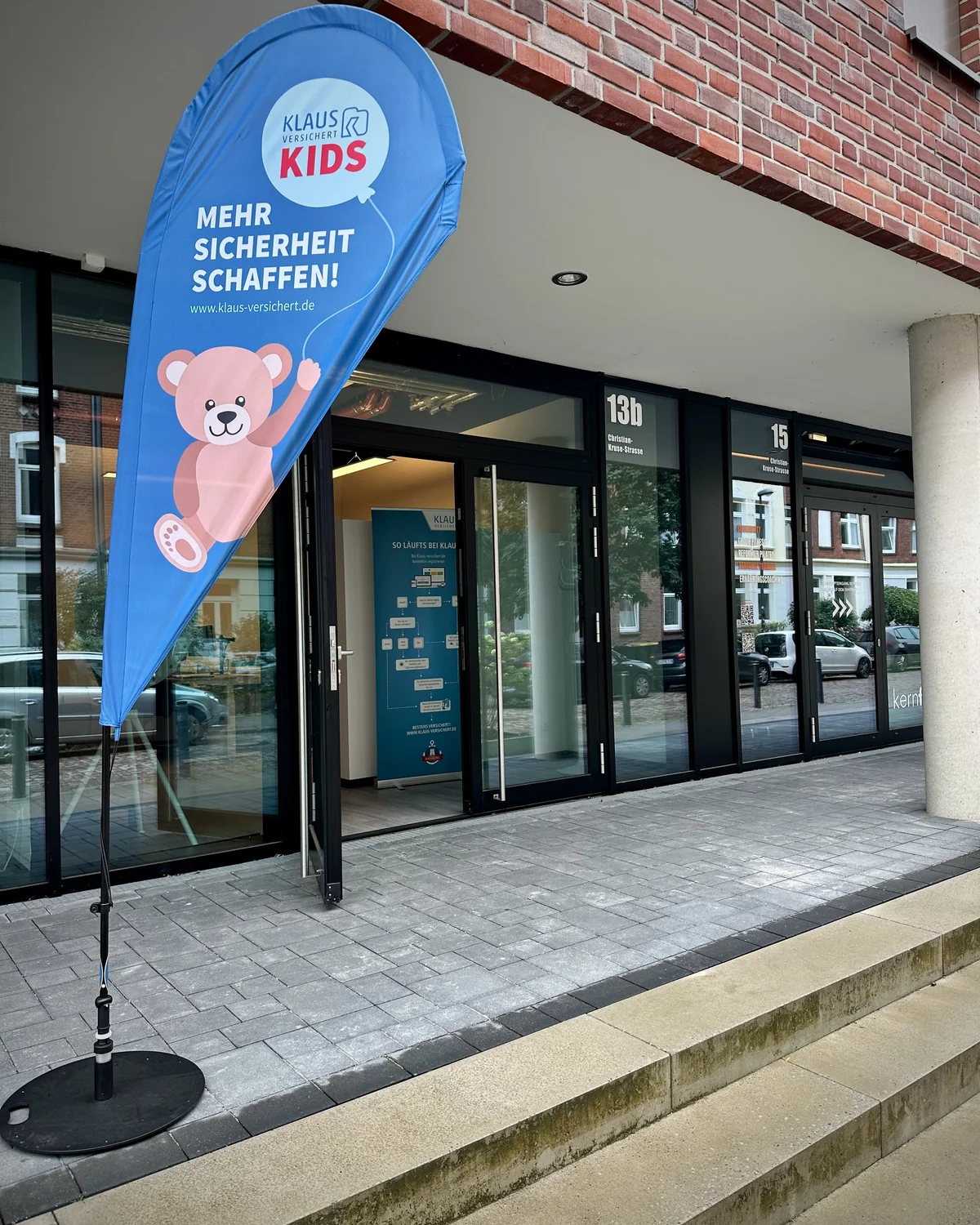 Eingang unseres Kieler Büros in der Christian-Kruse-Straße 13b mit geöffneter Glastür und Beachflag von Klaus versichert